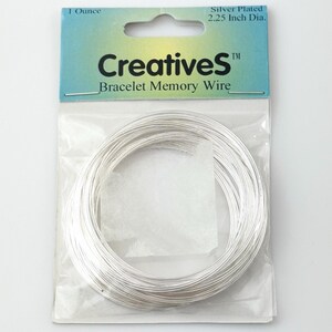 May include: A coil of silver-plated bracelet memory wire in a clear plastic bag with a blue and yellow header card. The packaging is labeled Creatives Bracelet Memory Wire, 1 Ounce, and 2.25 Inch Dia. The wire is thin, metallic, and circular.