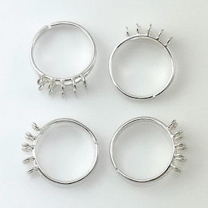May include: Four silver-colored rings, each with a unique design element. The rings are circular, with small, decorative protrusions extending from the band. The rings are set against a white background, highlighting their metallic sheen. These rings are ideal for jewelry making.