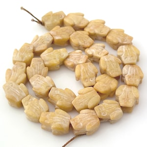May include: A strand of light yellow, carved stone beads shaped like small frogs. Each bead features a smooth, matte finish with subtle natural veining and a central hole for stringing. The beads are arranged in a loose, circular coil.