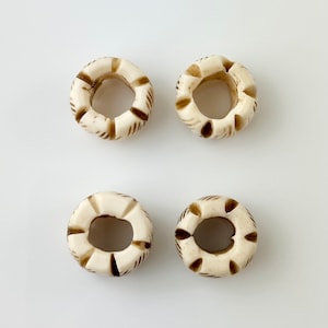 May include: Four white bone beads with brown carved designs. The beads are round with a hole in the center.