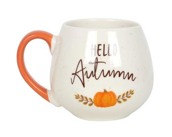 May include: White ceramic mug with an orange handle. The mug is decorated with the words "HELLO Autumn" in a script font, a pumpkin, and fall foliage. The mug is perfect for enjoying a warm beverage during the autumn season.