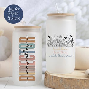 May include: Two frosted glass tumblers with lids and straws. One tumbler has the text "DIRECTOR mrs.colley" in colorful vertical letters. The other tumbler has the text "teach them love them watch them grow" with a floral design and butterflies.