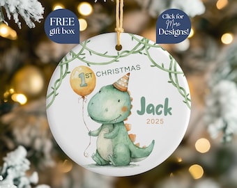 May include: A white ceramic Christmas ornament featuring a watercolor illustration of a green dinosaur holding a balloon. The ornament reads "1st Christmas" and "Jack 2025". Decorative vines surround the image.