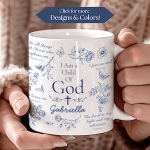 May include: White ceramic mug with blue floral designs and the text "I Am a Child of God Gabriella". The mug also features Bible verses and a cross. The mug is held by a person.