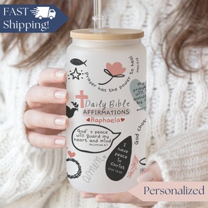 May include: A personalized frosted glass tumbler with a bamboo lid and straw. The tumbler is decorated with religious affirmations, a cross, and the name "Raphaela". The design includes various illustrations and text, with the words "Daily Bible Affirmations".