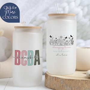 May include: Two frosted glass tumblers with bamboo lids and straws. One tumbler has the text "BCBA Campbell" in colorful letters. The other tumbler has the text "changing lives one behavior at a time" with a floral design.