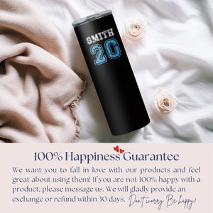 May include: Black tumbler with a white design that says "SMITH 20" in a blue font. The tumbler is sitting on a white and beige blanket. The text "100% Happiness Guarantee" is at the bottom of the image.