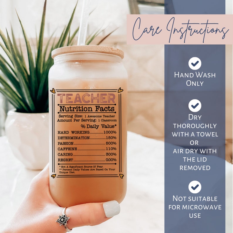 Puede incluir: Un vaso de vidrio transparente con una tapa de bamb&uacute; y un l&iacute;quido marr&oacute;n en su interior. El vaso tiene una etiqueta blanca con el texto "TEACHER Nutrition Facts" y una lista de valores nutricionales humor&iacute;sticos. El texto incluye "Hard Working 1000%", "Determination 150%", "Passion 500%", "Caffeine 110%", "Caring 300%" y "Regret 0.00%". El vaso est&aacute; sostenido por una mano con un anillo en el dedo. El fondo es una imagen borrosa de plantas verdes.