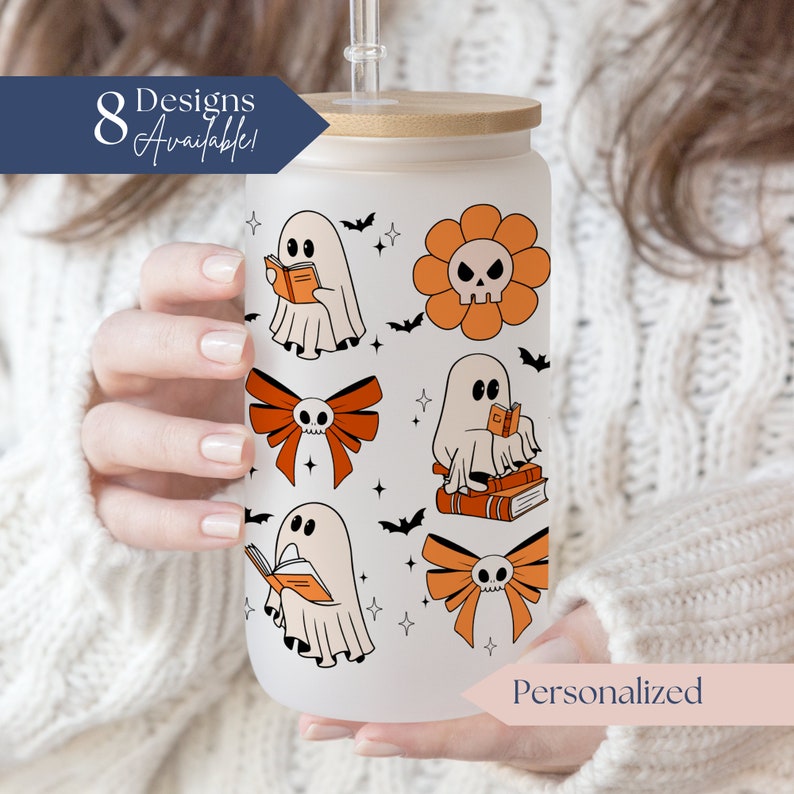 Op de afbeelding: Een matglazen beker met een bamboe deksel en rietje, met Halloween-thema ontwerpen. De ontwerpen omvatten geesten die boeken lezen, schedelbloemen en oranje strikken. Tekst op de beker luidt "8 Designs Available!" en "Personalized".