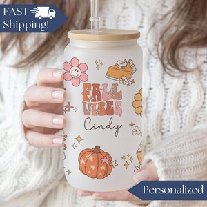 May include: Personalized frosted glass tumbler with a bamboo lid and straw. The tumbler features a fall-themed design with a pumpkin, pie, flowers, and the text "Fall Vibes" and "Cindy".