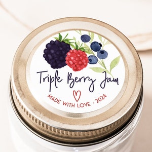 May include: A glass jar with a gold lid and a white label that says "Triple Berry Jam" with a red heart and the text "Made with Love - 2024". The label features a watercolor illustration of blackberries, raspberries, and blueberries.