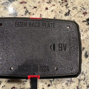 May include: Black rectangular back plate with the text "EEOM BACK PLATE" and "MADE IN USA". The plate has a textured surface and a red accent. A 9V battery symbol is visible.