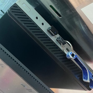 May include: A black and silver electronic device with a Netgear adapter and a blue and silver bottle opener attached. The device is mounted on a metal surface.