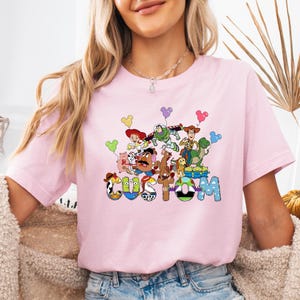 A woman wearing a pink t-shirt with a colorful graphic of characters from the Toy Story franchise.