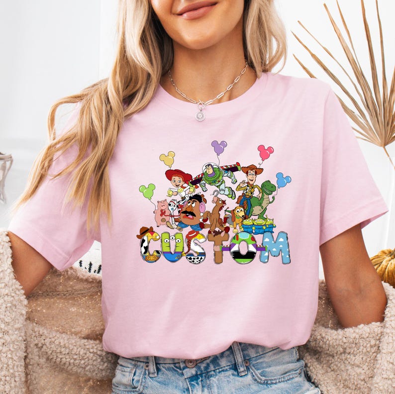 A woman wearing a pink t-shirt with a colorful graphic of characters from the Toy Story franchise.