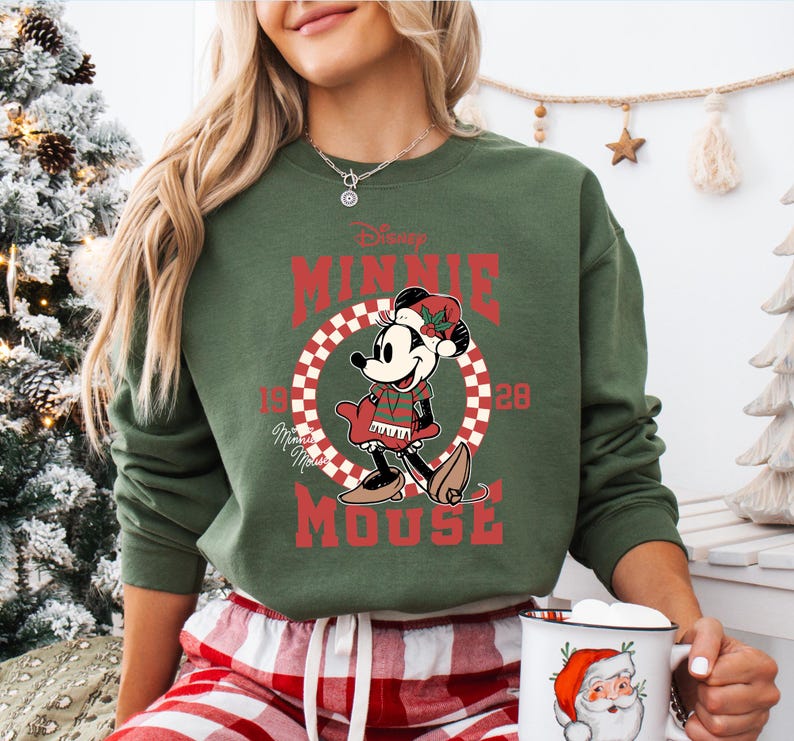 A woman wearing a green sweatshirt with a Minnie Mouse graphic and holding a mug with a Santa Claus design.