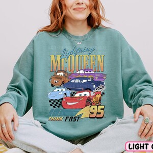 a woman sitting on a bed wearing a sweatshirt with cars on it