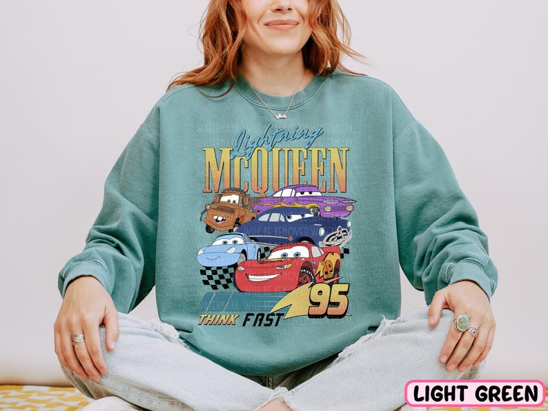 a woman sitting on a bed wearing a sweatshirt with cars on it