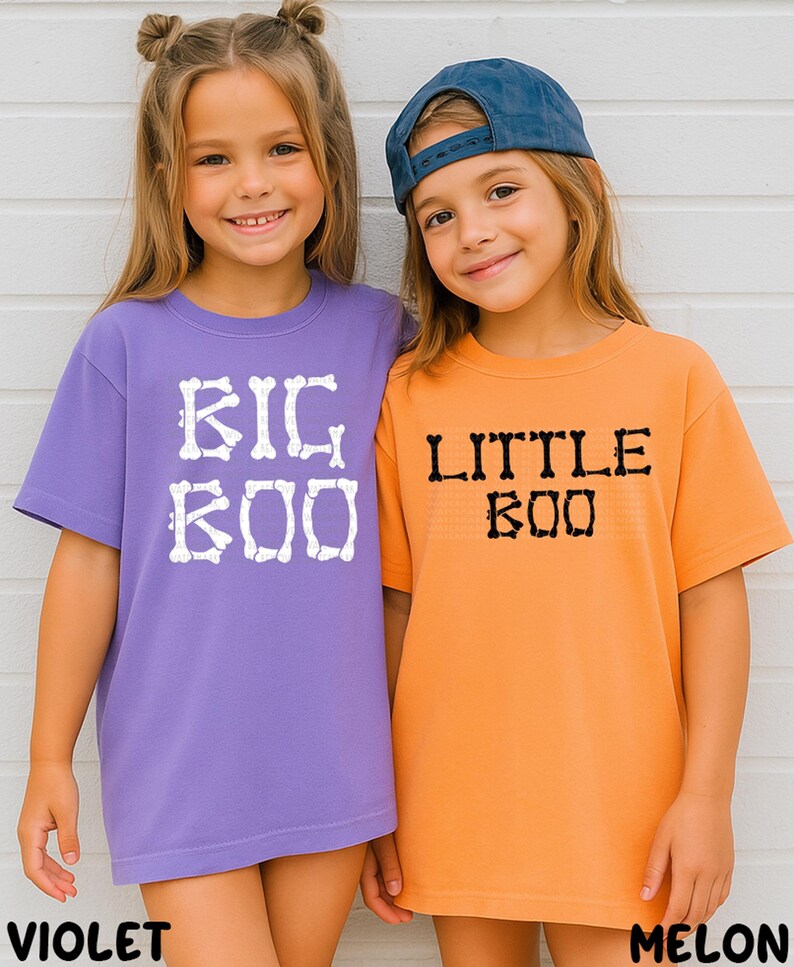 Two young girls wearing purple and orange t-shirts with the text "BIG BOO" and "LITTLE BOO" printed on them, respectively.