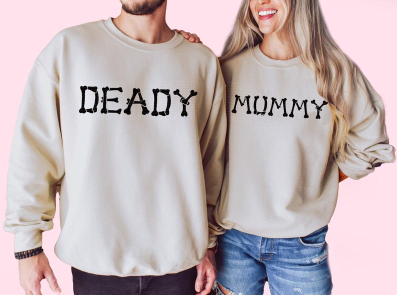 A man and a woman standing side by side, both wearing matching beige sweatshirts with the word "DEADY" printed on them.