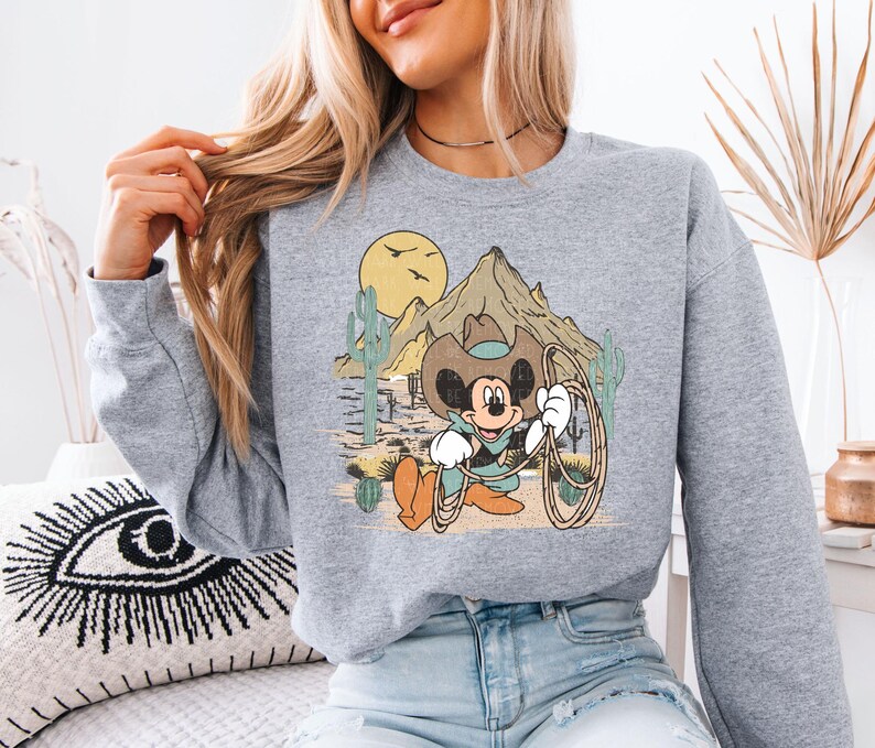 a woman sitting on a bed wearing a mickey mouse sweatshirt