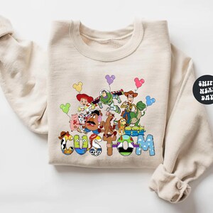 A beige sweatshirt with a colorful graphic design featuring characters from the Toy Story movie, including Woody, Buzz Lightyear, and other beloved characters.