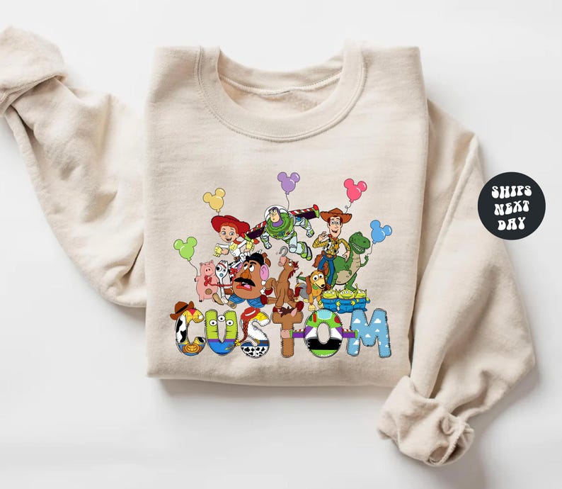 A beige sweatshirt with a colorful graphic design featuring characters from the Toy Story movie, including Woody, Buzz Lightyear, and other beloved characters.
