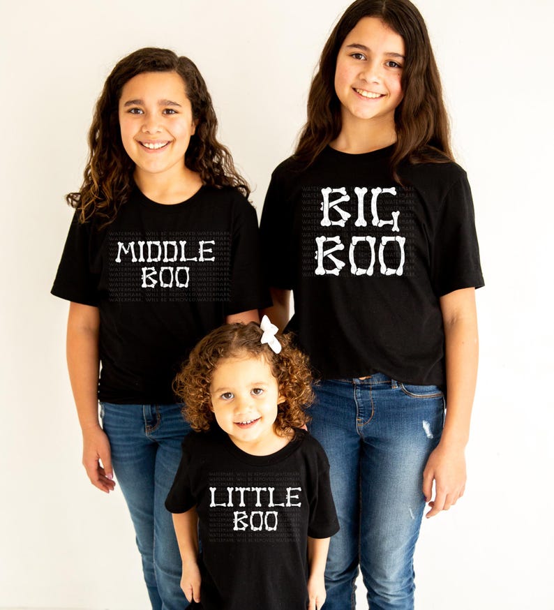 Three young girls wearing black t-shirts with the text "MIDDLE BOO" and "BIG BOO" printed on them, standing together and smiling.