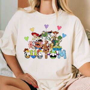 A white t-shirt with a colorful graphic design featuring characters from the Toy Story movie, including Woody, Buzz Lightyear, and other beloved characters.