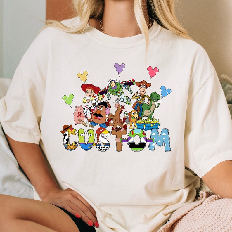 A white t-shirt with a colorful graphic design featuring characters from the Toy Story movie, including Woody, Buzz Lightyear, and other beloved characters.