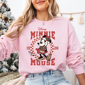 A woman wearing a pink sweatshirt with a cartoon image of Minnie Mouse and the text "Disney Minnie Mouse" printed on it.