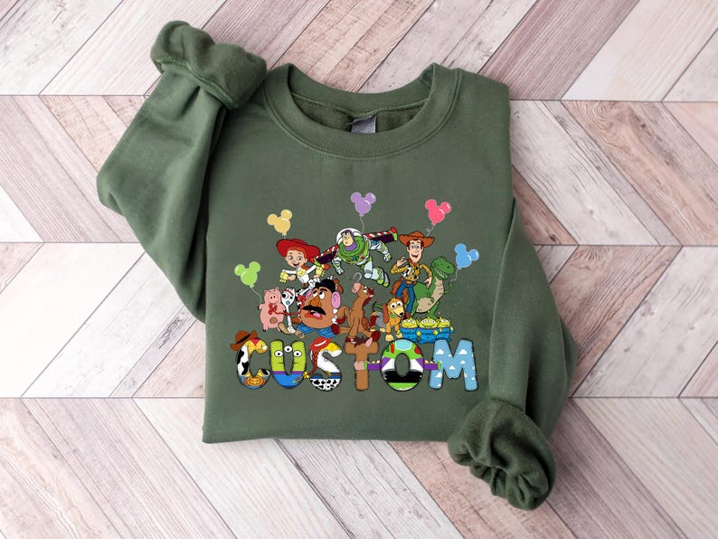 A green sweatshirt with a colorful graphic of characters from the Toy Story movie, including Woody, Buzz Lightyear, and other beloved characters.