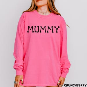 A woman wearing a pink long-sleeved shirt with the word "MUMMY" printed on it.