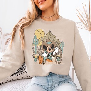 a woman sitting on a bed wearing a mickey mouse sweatshirt