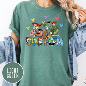 A green t-shirt with a colorful graphic design featuring characters from the Toy Story franchise, including Woody, Buzz Lightyear, and other beloved characters.