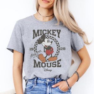 A woman wearing a gray t-shirt with a Mickey Mouse graphic and text, smiling at the camera.