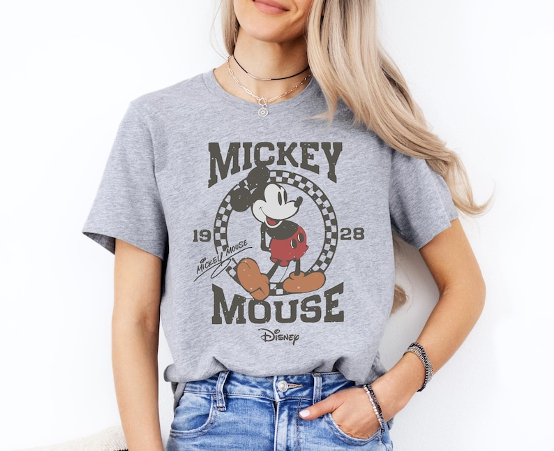 A woman wearing a gray t-shirt with a Mickey Mouse graphic and text, smiling at the camera.