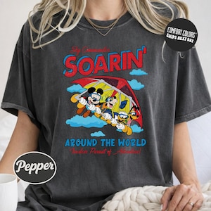 A person wearing a gray t-shirt with a graphic design featuring Mickey Mouse and Goofy characters flying in a hot air balloon.