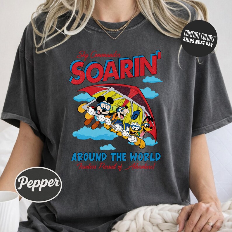 A person wearing a gray t-shirt with a graphic design featuring Mickey Mouse and Goofy characters flying in a hot air balloon.