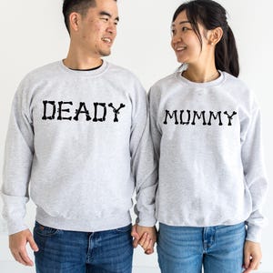 A man and a woman standing side by side, both wearing gray sweatshirts with the word "DEADY" printed on them.