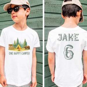 a young boy wearing a white shirt with a camp scene on it