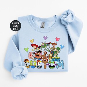 A light blue long-sleeved shirt with a colorful graphic design featuring characters from the Toy Story franchise.