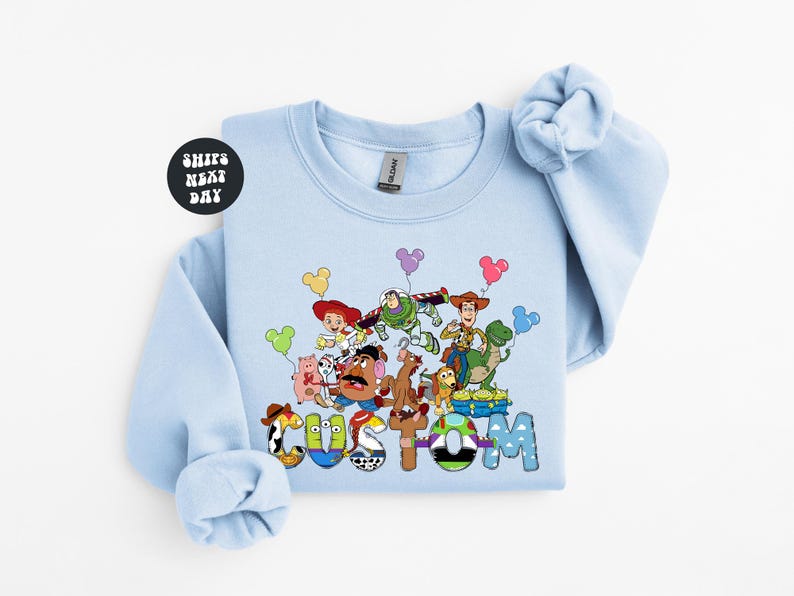 A light blue long-sleeved shirt with a colorful graphic design featuring characters from the Toy Story franchise.