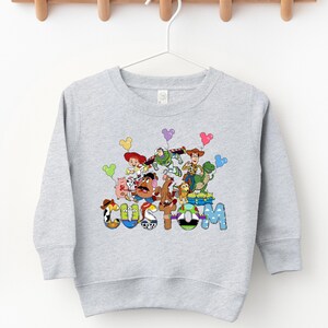 A gray sweatshirt with a colorful graphic design featuring various cartoon characters and the word "COSM" prominently displayed.