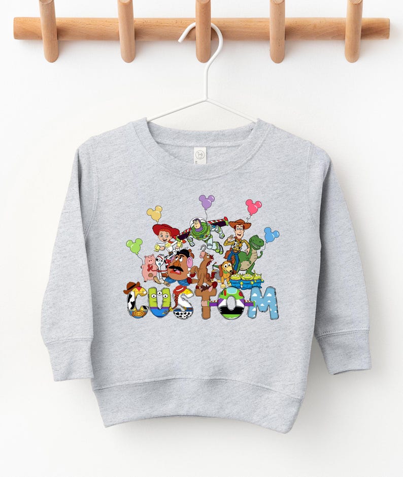 A gray sweatshirt with a colorful graphic design featuring various cartoon characters and the word "COSM" prominently displayed.