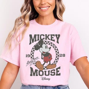 A woman wearing a pink t-shirt with a Mickey Mouse graphic and text, smiling at the camera.