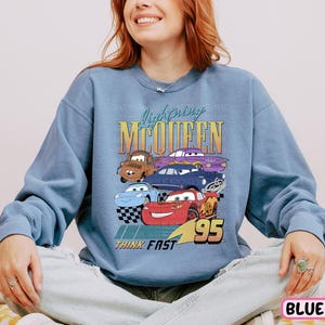 a woman sitting on a bed wearing a blue sweatshirt