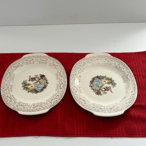 May include: Two oval-shaped white ceramic plates with gold trim and a floral design. Each plate features a central image of a couple in a garden setting.