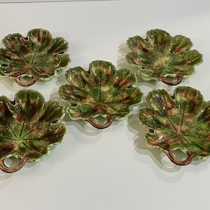 May include: Set of five green and brown ceramic leaf-shaped serving dishes with handles. Each dish is shaped like a leaf with a raised vein pattern and a brown handle.