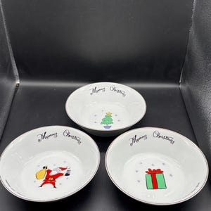 May include: Three white ceramic bowls with a gold rim and the words "Mommy Christmas" in cursive. Each bowl features a different Christmas-themed illustration: a Christmas tree, Santa Claus, and a wrapped gift.